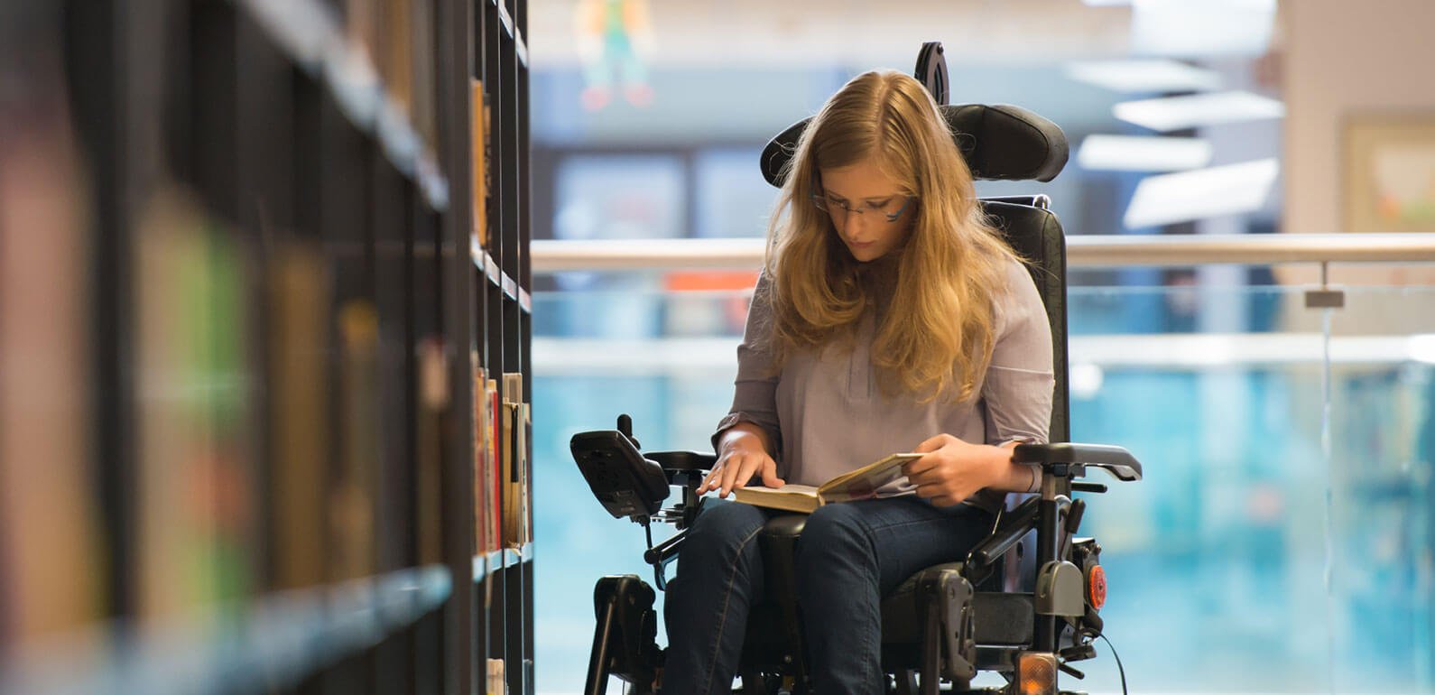 An adult female in a wheelchair in a library reading