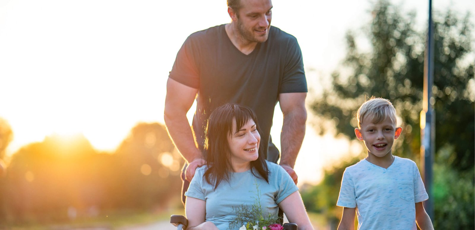 Man pushing a women in a wheelchair. The woman is holding hands with a child