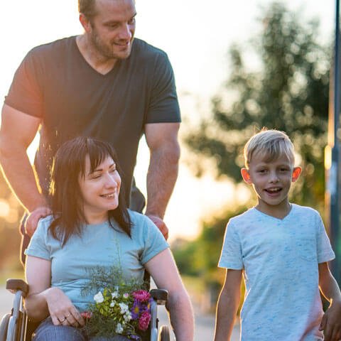 Man pushing a women in a wheelchair. The woman is holding hands with a child